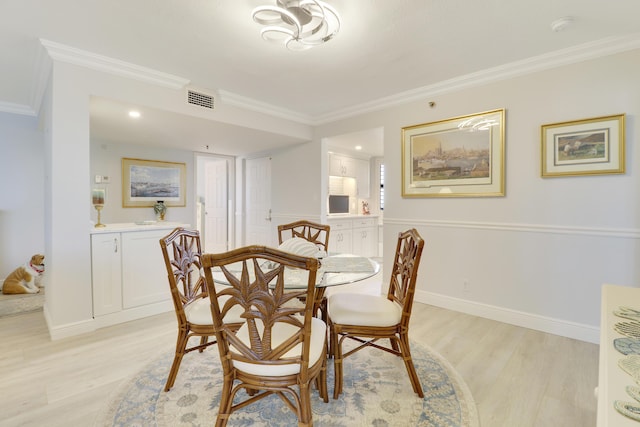 dining room featuring baseboards, visible vents, light wood finished floors, and ornamental molding