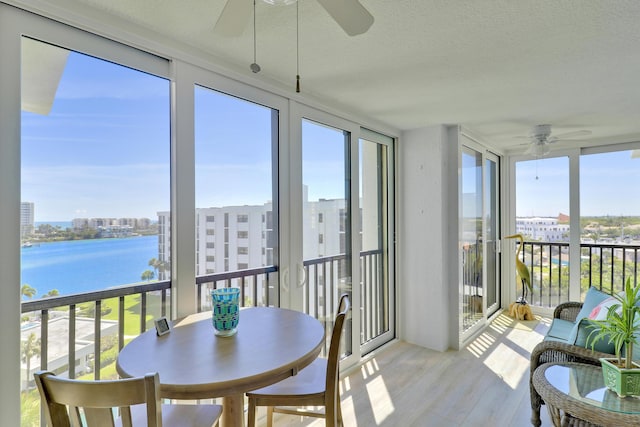 sunroom featuring a view of city, a ceiling fan, and a water view