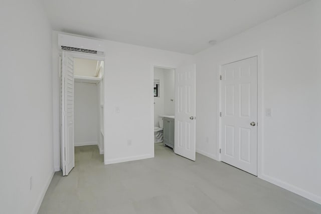 unfurnished bedroom with a walk in closet, a closet, baseboards, and a wall mounted air conditioner