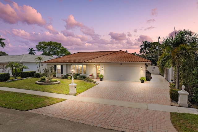 mediterranean / spanish house with a yard, stucco siding, a garage, a tile roof, and decorative driveway