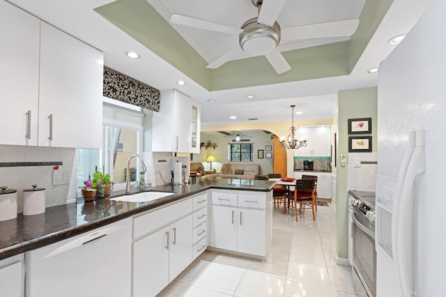 kitchen with a tray ceiling, ceiling fan with notable chandelier, a peninsula, white appliances, and a sink