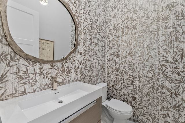 bathroom featuring toilet, vanity, and wallpapered walls