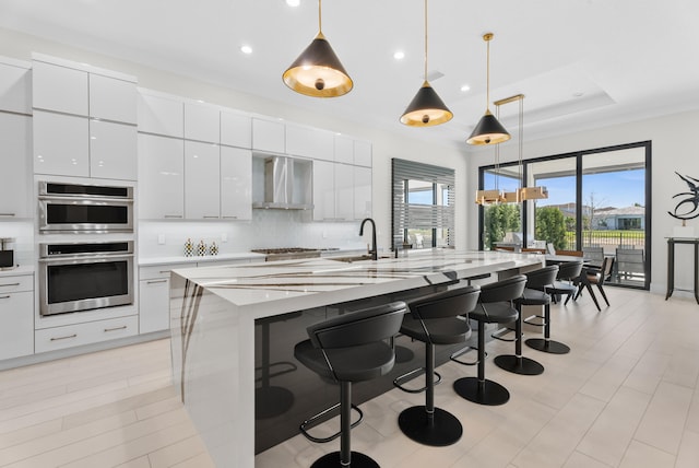 kitchen with wall chimney range hood, decorative backsplash, white cabinets, a kitchen breakfast bar, and modern cabinets