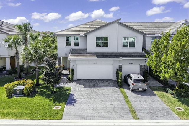 view of front of home featuring a tile roof, a front yard, stucco siding, decorative driveway, and an attached garage