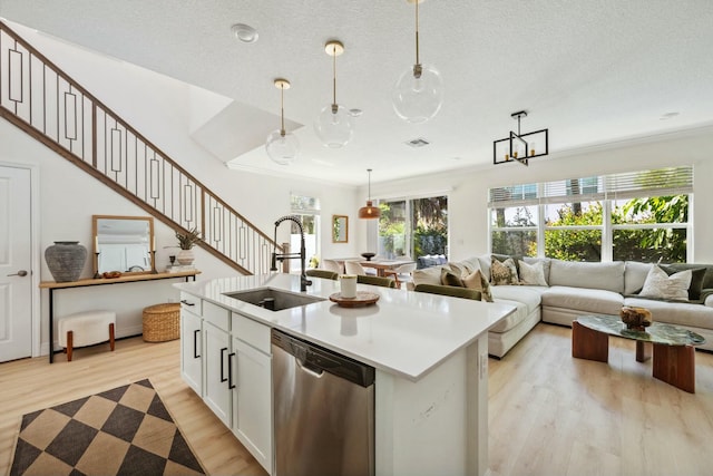 kitchen featuring visible vents, dishwasher, light wood-style flooring, hanging light fixtures, and a sink