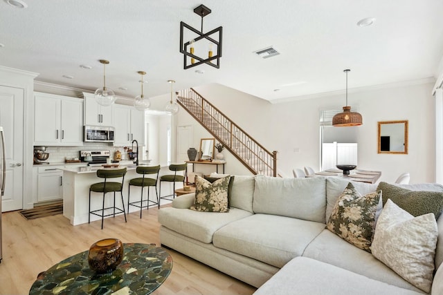 living room with visible vents, light wood-style floors, and ornamental molding