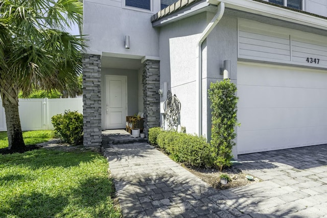 doorway to property with fence, stucco siding, a garage, stone siding, and a gate