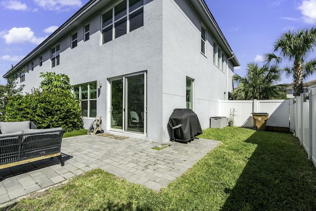 rear view of house with stucco siding, a lawn, and a patio area