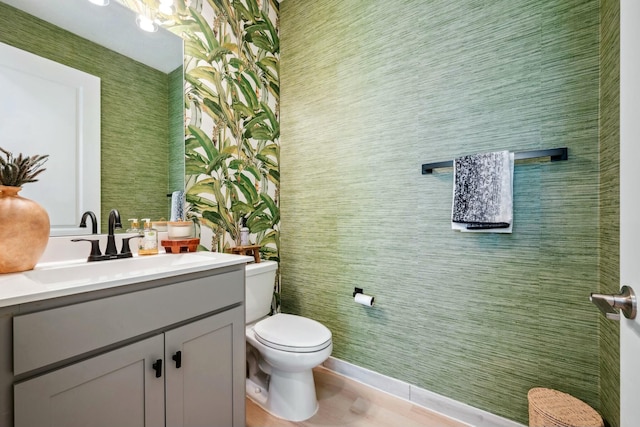 half bathroom with vanity, toilet, and wallpapered walls