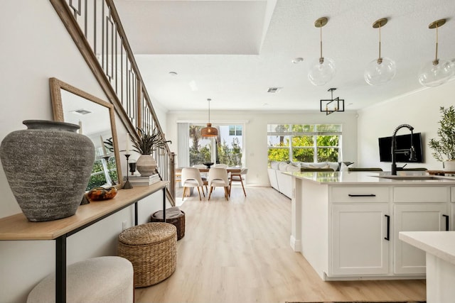 kitchen with light countertops, white cabinetry, crown molding, decorative light fixtures, and light wood-type flooring