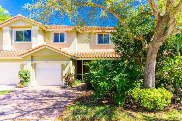 mediterranean / spanish house with decorative driveway, a garage, a tile roof, and stucco siding