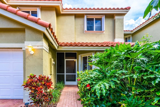 doorway to property featuring a tiled roof, a garage, and stucco siding