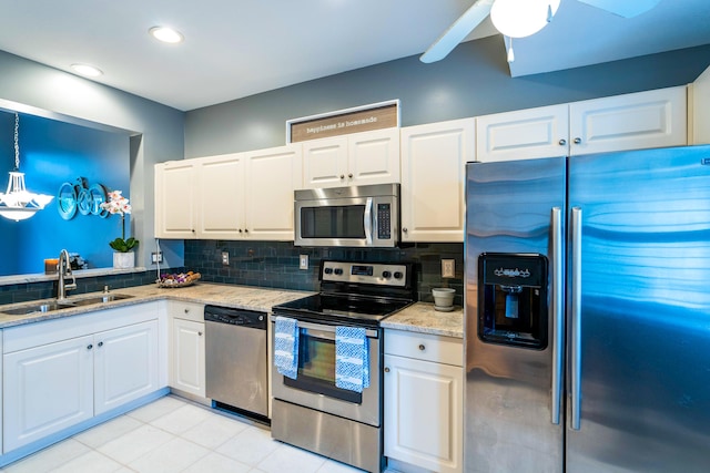 kitchen featuring light stone counters, decorative backsplash, appliances with stainless steel finishes, white cabinetry, and a sink