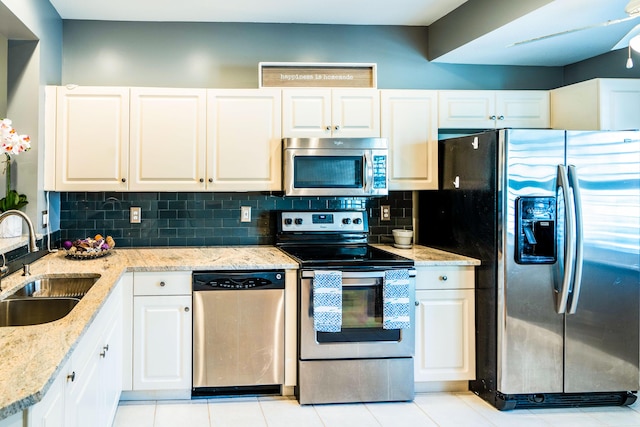 kitchen featuring light stone countertops, decorative backsplash, appliances with stainless steel finishes, white cabinets, and a sink