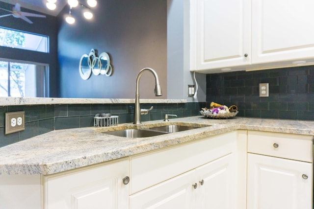 kitchen with white cabinetry, light stone countertops, backsplash, and a sink