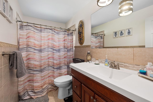 full bath with toilet, vanity, wainscoting, tile patterned floors, and tile walls