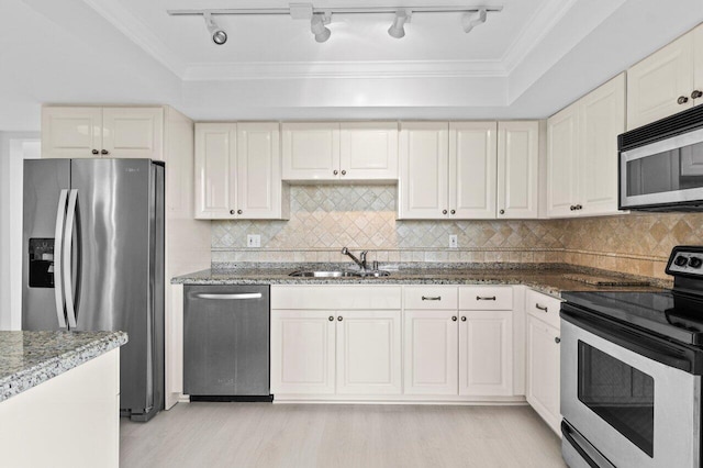 kitchen featuring crown molding, dark stone counters, light wood-style floors, stainless steel appliances, and a sink