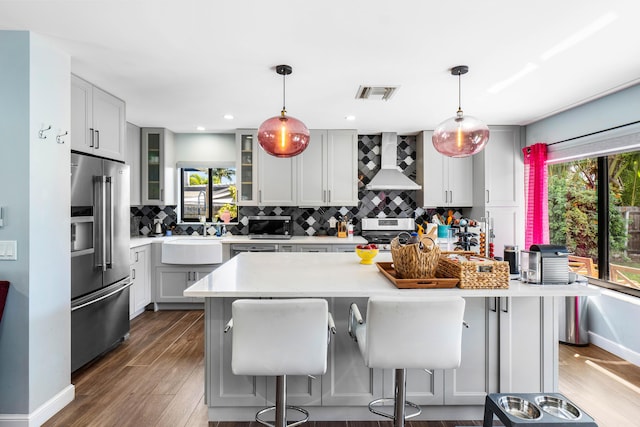 kitchen featuring visible vents, a sink, appliances with stainless steel finishes, wall chimney exhaust hood, and decorative backsplash