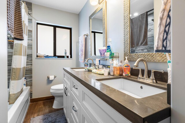 full bath featuring double vanity, toilet, wood finished floors, and a sink