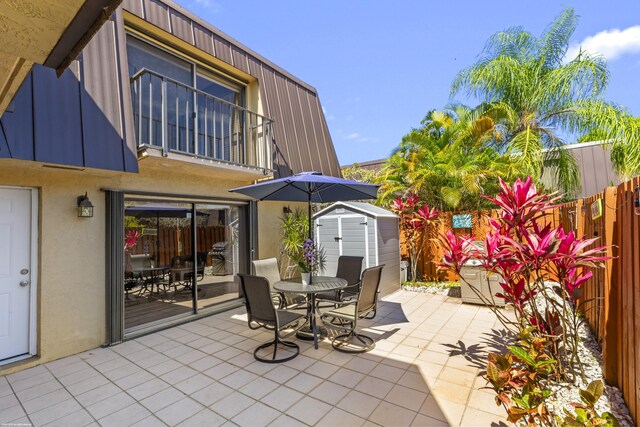 view of patio featuring outdoor dining area, a fenced backyard, a balcony, a storage shed, and an outdoor structure