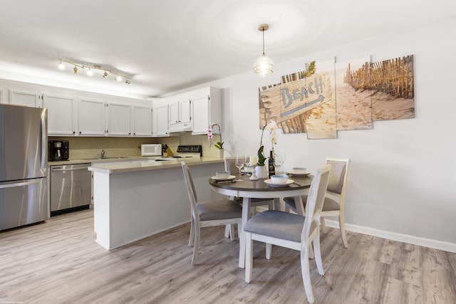 kitchen featuring baseboards, light wood finished floors, a peninsula, light countertops, and appliances with stainless steel finishes