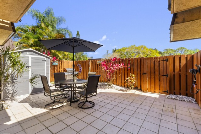 view of patio with an outdoor structure, a fenced backyard, outdoor dining space, a storage unit, and a gate