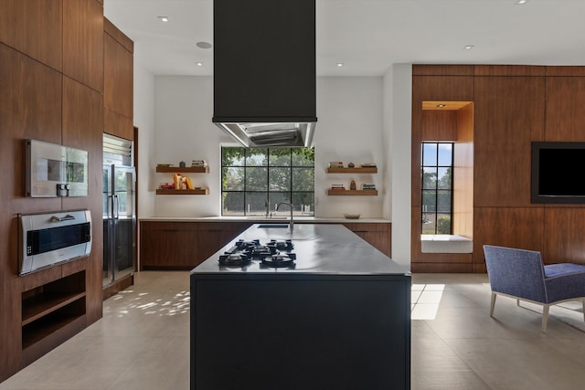 kitchen featuring stainless steel microwave, open shelves, light tile patterned floors, modern cabinets, and a kitchen island with sink