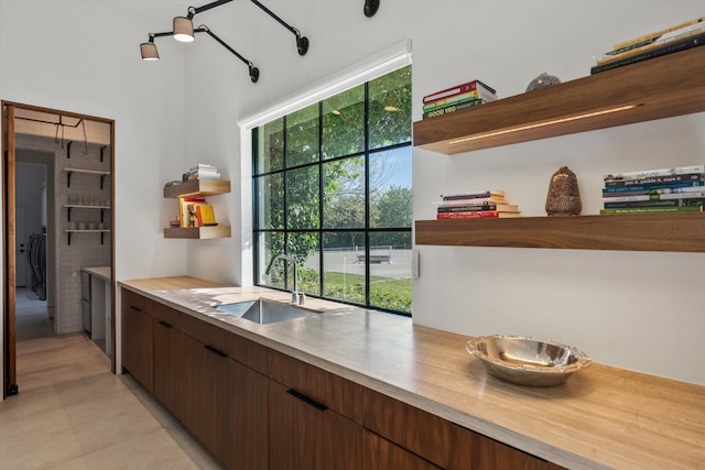 kitchen with open shelves, light countertops, dark brown cabinetry, and a sink