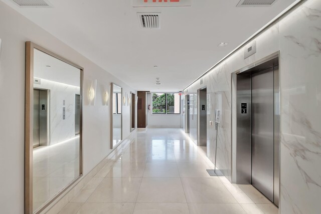 hallway with elevator, visible vents, and light tile patterned floors