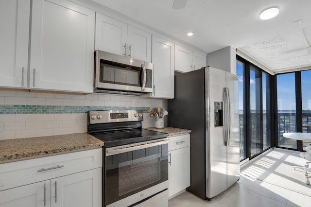 kitchen with tasteful backsplash, expansive windows, light stone counters, appliances with stainless steel finishes, and white cabinets