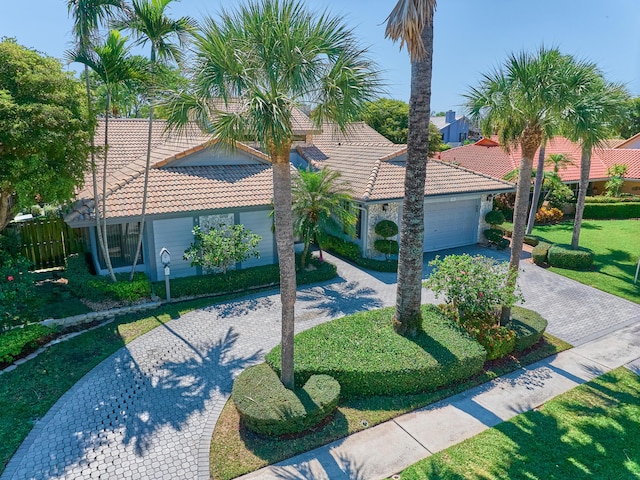 mediterranean / spanish house featuring stucco siding, decorative driveway, a front yard, a tile roof, and an attached garage