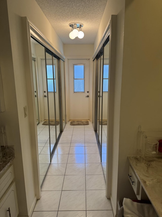 hall with a textured ceiling, baseboards, and light tile patterned flooring