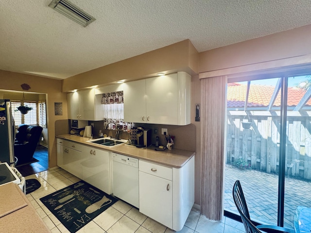 kitchen with visible vents, white dishwasher, a sink, freestanding refrigerator, and white cabinetry