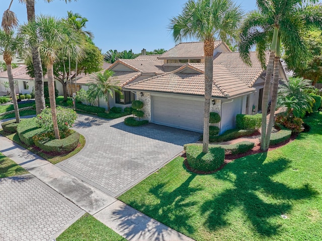 mediterranean / spanish home with an attached garage, a tile roof, stucco siding, a front lawn, and decorative driveway