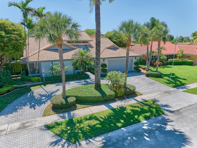 view of front of home with an attached garage, a front lawn, curved driveway, and a tile roof