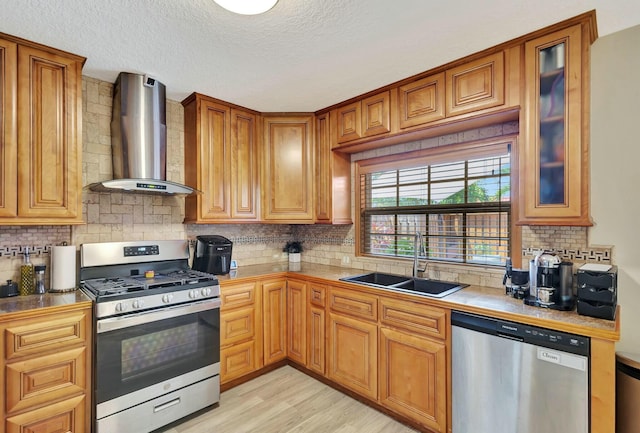 kitchen featuring light wood-type flooring, a sink, appliances with stainless steel finishes, wall chimney exhaust hood, and glass insert cabinets