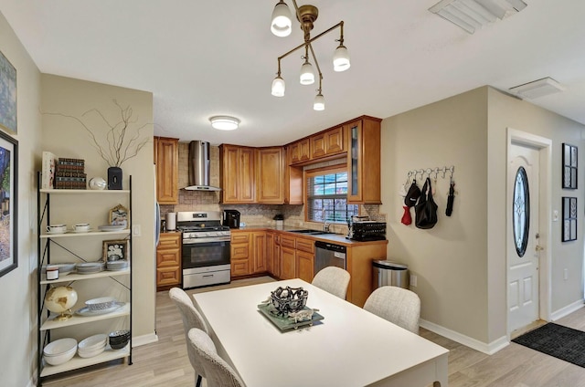 kitchen featuring light wood-type flooring, stainless steel appliances, wall chimney exhaust hood, and decorative backsplash