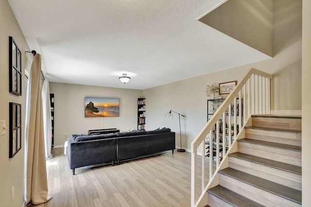 living room featuring stairway, baseboards, a textured ceiling, and wood finished floors