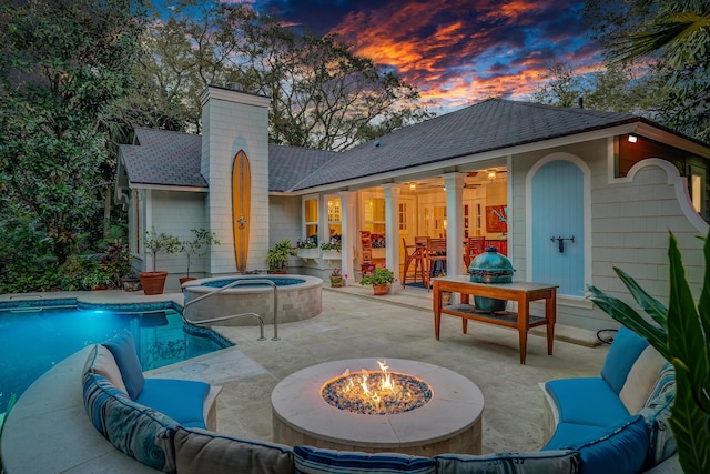 back of house featuring an in ground hot tub, an outdoor pool, a shingled roof, an outdoor living space with a fire pit, and a patio area