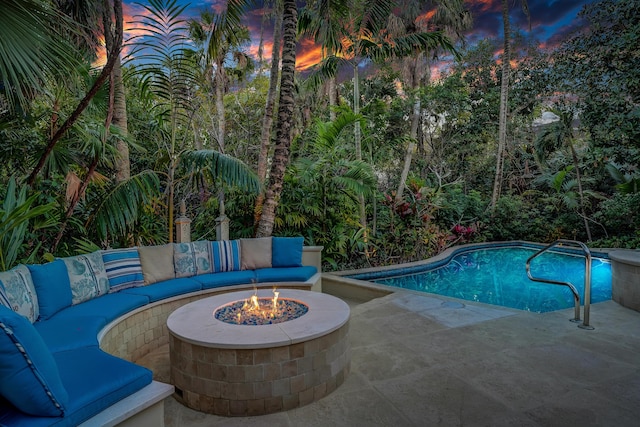 pool at dusk with a patio area, an outdoor pool, and an outdoor living space with a fire pit