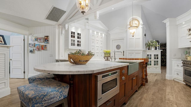 kitchen with visible vents, stainless steel microwave, lofted ceiling, light wood-style flooring, and a sink