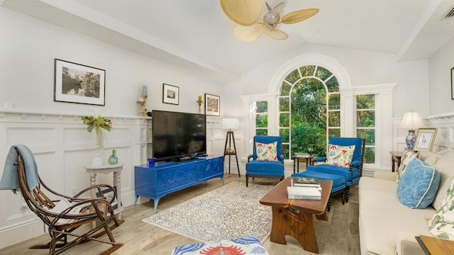 living area featuring ceiling fan, a wainscoted wall, vaulted ceiling, wood finished floors, and a decorative wall