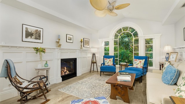 living area with a glass covered fireplace, a decorative wall, lofted ceiling, and wood finished floors