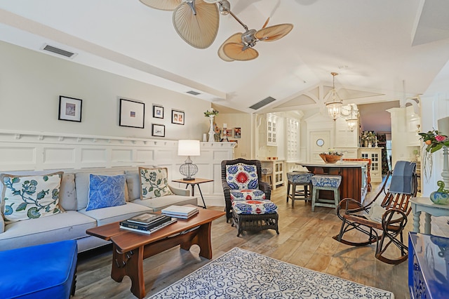 living area with visible vents, ceiling fan with notable chandelier, light wood-type flooring, and vaulted ceiling