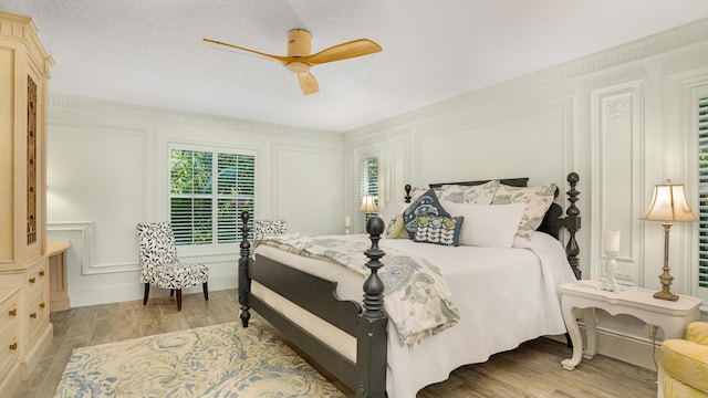 bedroom with ceiling fan, a textured ceiling, light wood-style flooring, and a decorative wall