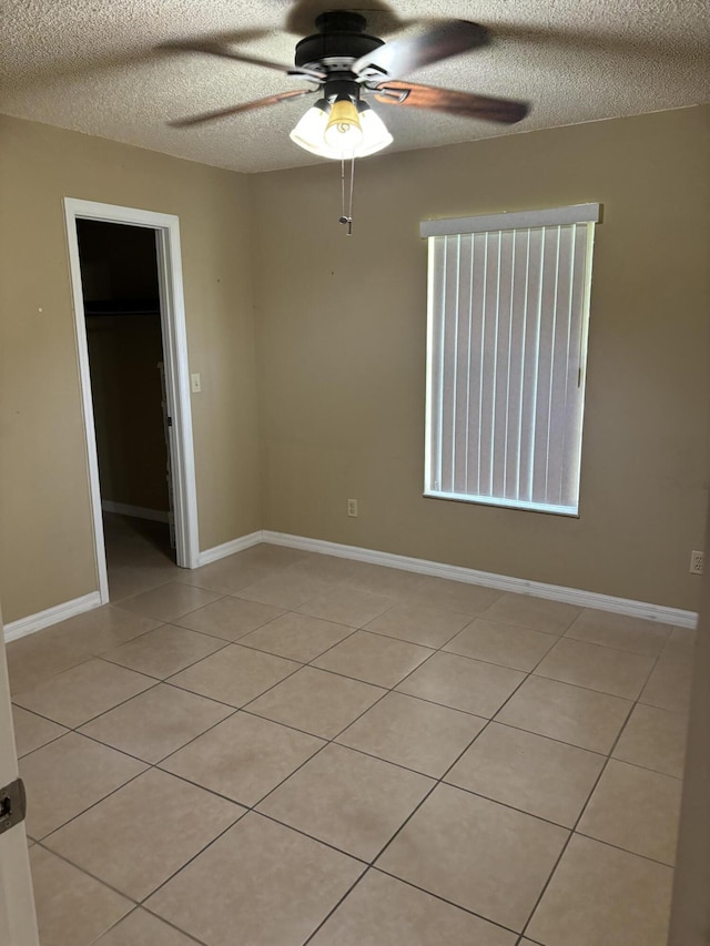 spare room featuring light tile patterned flooring, ceiling fan, a textured ceiling, and baseboards