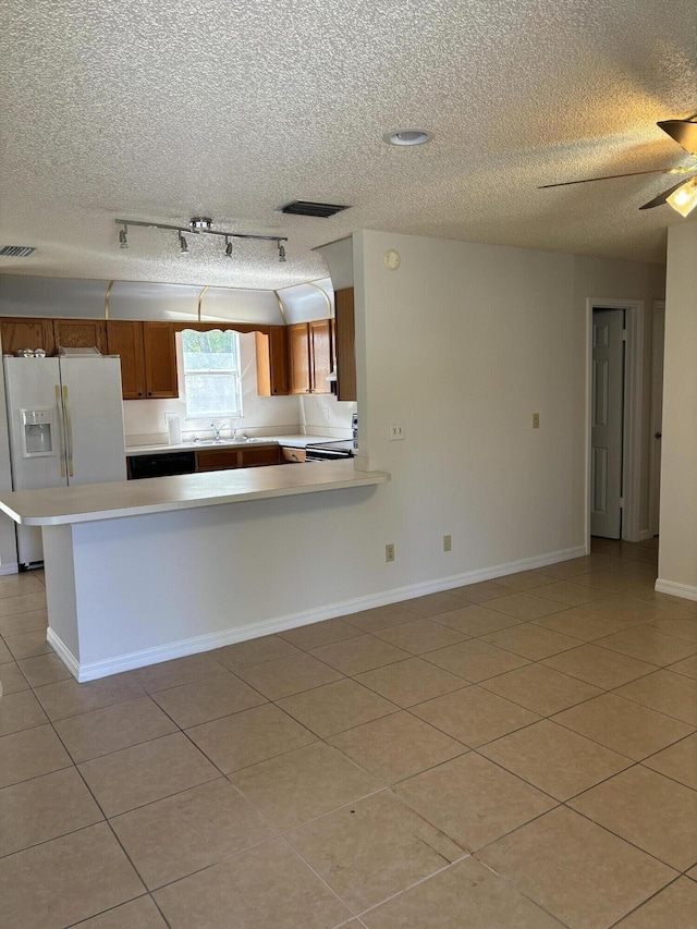 kitchen featuring visible vents, ceiling fan, light countertops, white refrigerator with ice dispenser, and brown cabinetry