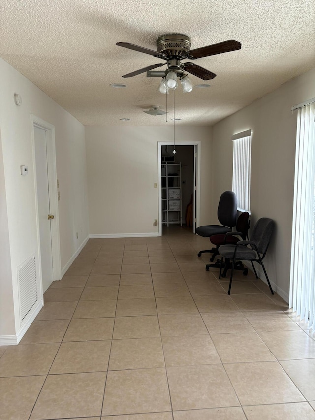 living area featuring baseboards, visible vents, light tile patterned flooring, ceiling fan, and a textured ceiling