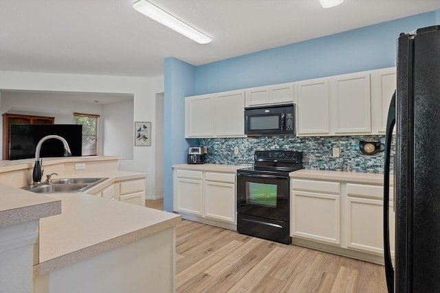 kitchen featuring tasteful backsplash, light countertops, light wood-style flooring, black appliances, and a sink