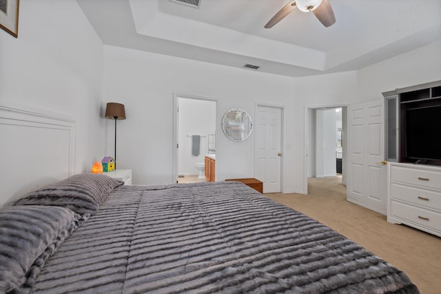 carpeted bedroom with ceiling fan, visible vents, a raised ceiling, and ensuite bath